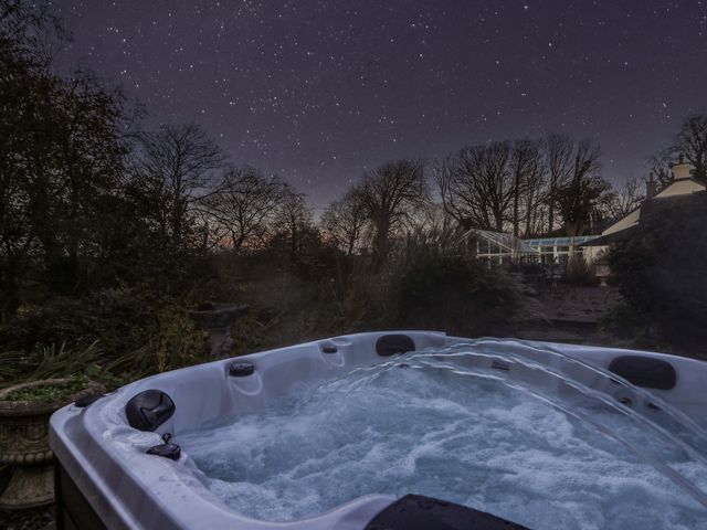 An outdoor hot tub with bubbling water surrounded by trees and plants under a starry night sky at St Dogwells Barn near Wolfscastle