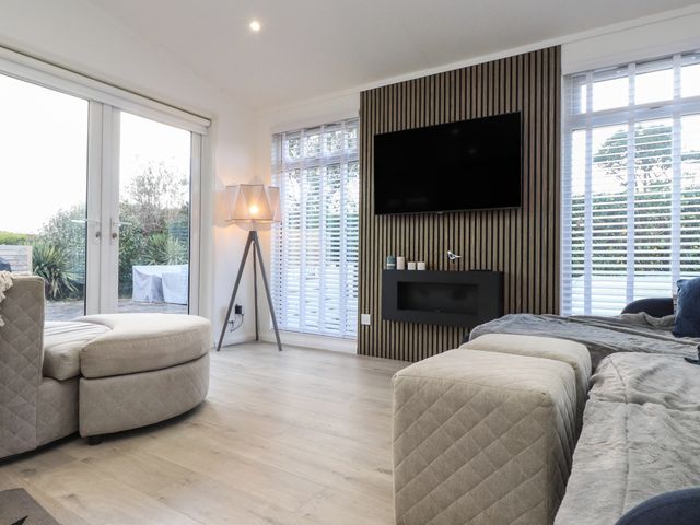 A living room with a wall mounted TV and a floor lamp near windows with blinds at The Warren M5 in Castellmarch near Abersoch