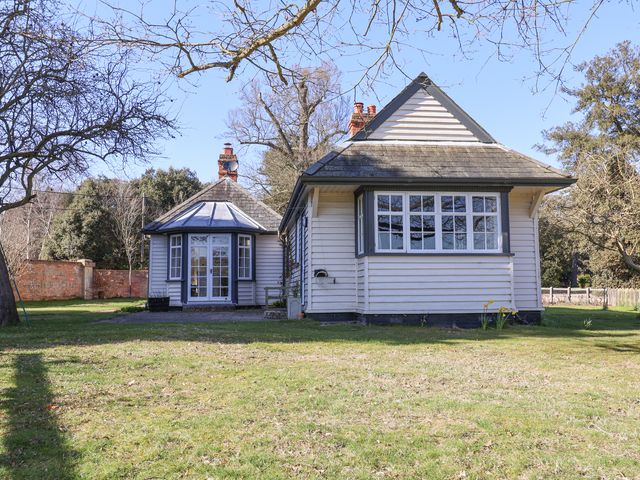 A house with white wooden siding and multiple windows surrounded by trees and grass at Holm Oak Lodge in Tendring near Weeley