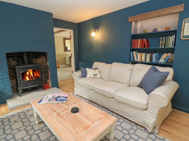 A living room with a beige sofa next to a fireplace and a wooden coffee table with magazines at Kingfishers in Little Clanfield near Bampton