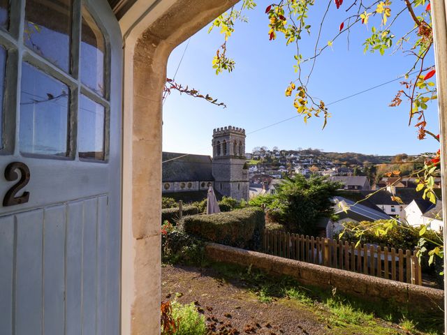 A partially open blue door with the number 2 looking out to a garden hedge a wooden fence a church tower and houses on a hill at Barley Cottage in Beer