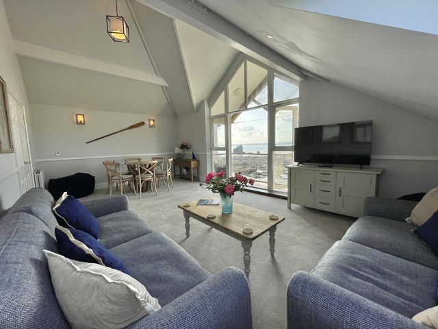A living room with two sofas a coffee table a dining table and large windows with a sea view at 12 Thurlestone Rock in Thurlestone