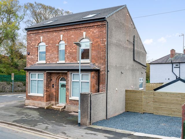 A two-story brick house with a green front door and white framed windows next to a gravel driveway and wooden fence at Lund House in Ulverston