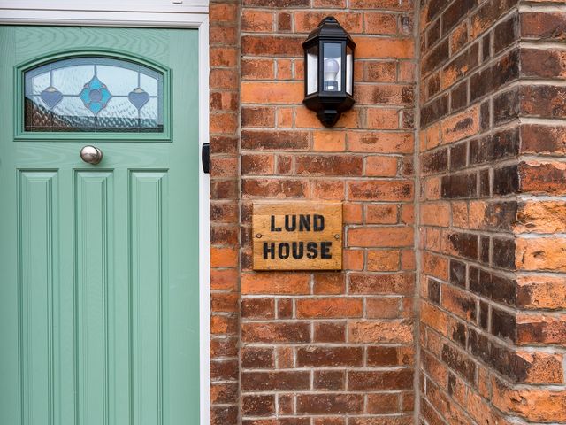 A green front door next to a wooden sign that says Lund House mounted on a brick wall with a black outdoor light above it at Lund House in Ulverston