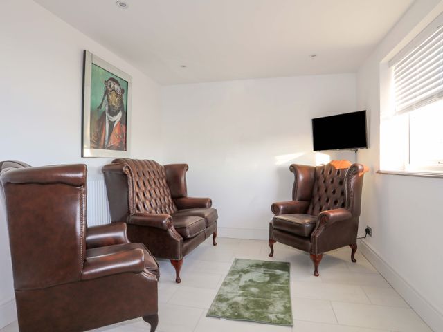 A small sitting room with three brown leather armchairs a green rug a wall-mounted TV and a framed picture at Ty'n Ffridd Bach in Chwilog near Y Ffor