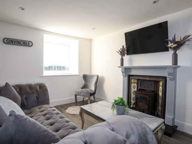 A living room with a gray sofa, armchair, marble coffee table, fireplace with a TV above and decorative plants at Ty'n Ffridd in Chwilog near Criccieth