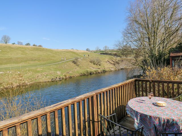A wooden balcony overlooking a river with a table covered by a patterned cloth and two glasses at Kirk Yett Cottage in Linton Falls