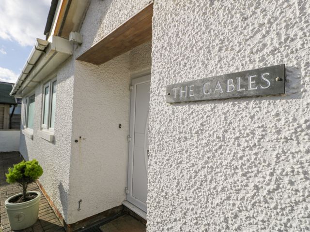 A front entrance with a white door and a sign reading The Gables on a textured wall with a small potted plant outside at The Gables in Tywyn