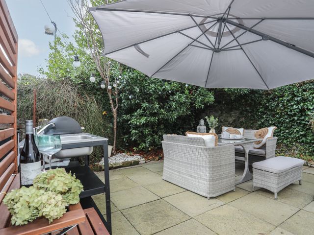An outdoor patio with a table and chairs under a large umbrella and a barbecue grill at Gweryl Lodge in Conwy