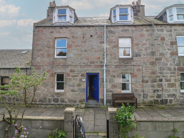 A stone house exterior with a blue front door at Footdee Cottage in Aberdeen