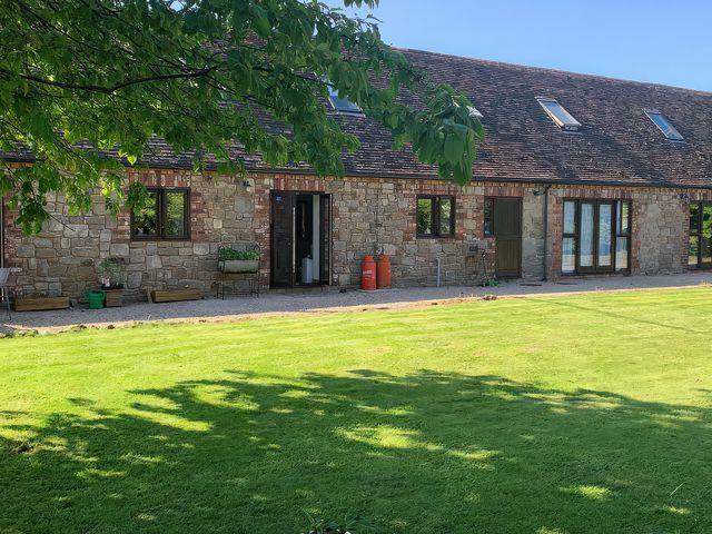An outdoor view of a stone building with green grass and seating at Upper Home Farm