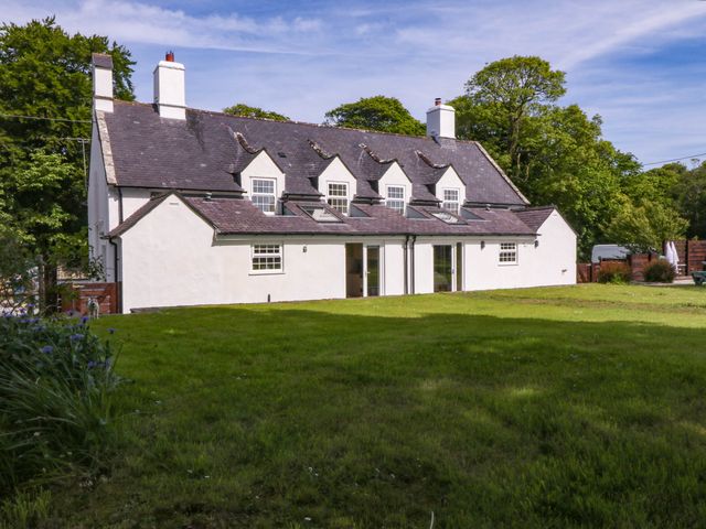 A white house with a dark roof and lawn in front surrounded by trees at Bodior Garden Cottage in Rhoscolyn