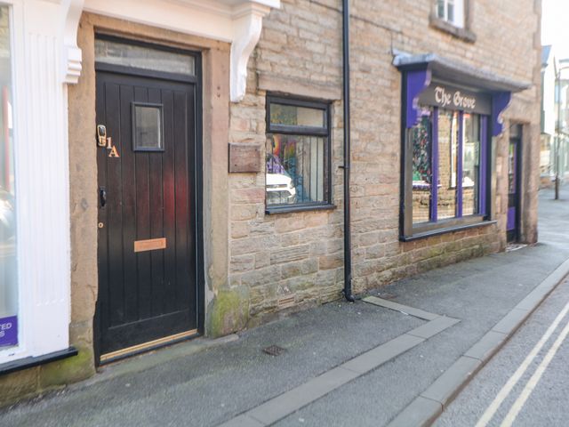 A black door with number 1A beside a stone wall building with a window and a shop called The Grove with purple trim at 1A Market Street in Buxton