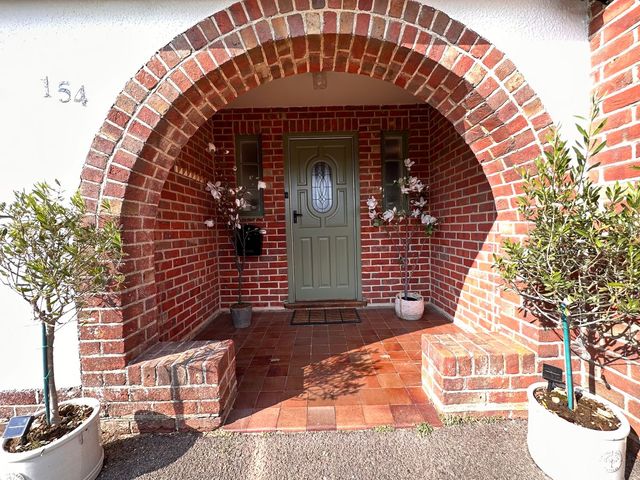 A brick arched porch with a green front door and potted plants on either side at Bayview Cottage in Southbourne
