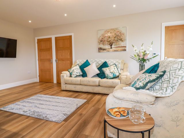 A living room with two sofas, cushions, a small table with croissants and glass cups, a rug, wooden doors, a wall-mounted TV, and a painting at Little Hillside in Redruth