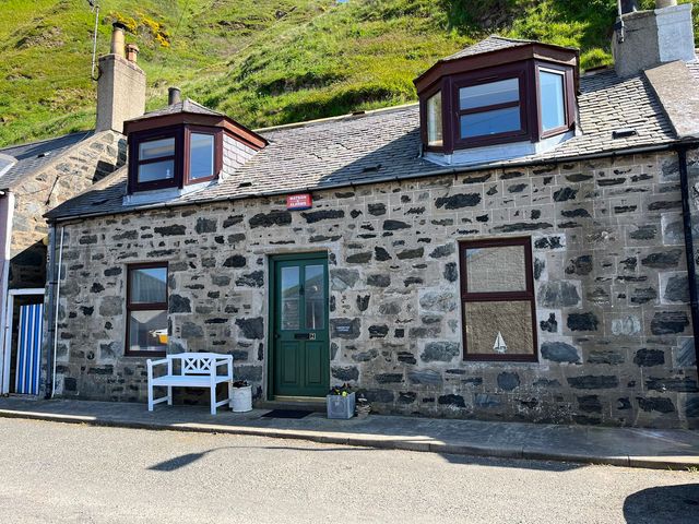 Stone cottage with green door white bench and flower pots on a street at Lobster Pot in Gardenstown