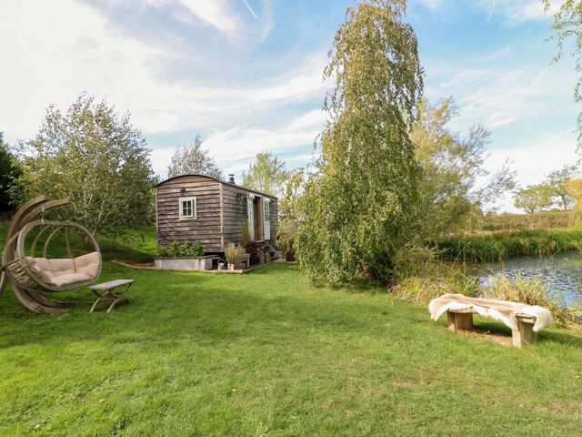 A wooden hut and seating area beside a pond at Herbie's Shepherds Hut at Shepherds Lodge Retreat and Wellness Bottesford near Redmile and Vale of Belvoir