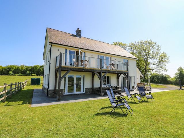 A two-story house with a wooden balcony and patio chairs on a lawn at Yr Adfa in Llangeitho near Tregaron