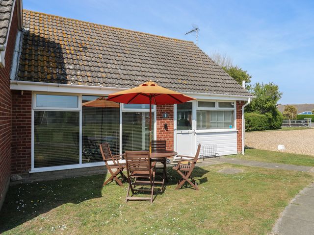 A patio area with a round wooden table and four chairs with an orange umbrella outside a brick house with a tiled roof at 1 Kessingland Cottages in Kessingland