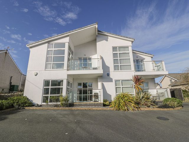 A modern white two-story house with large windows and glass balconies with shrubs and plants in front at Seaview in Benllech near Red Wharf Bay