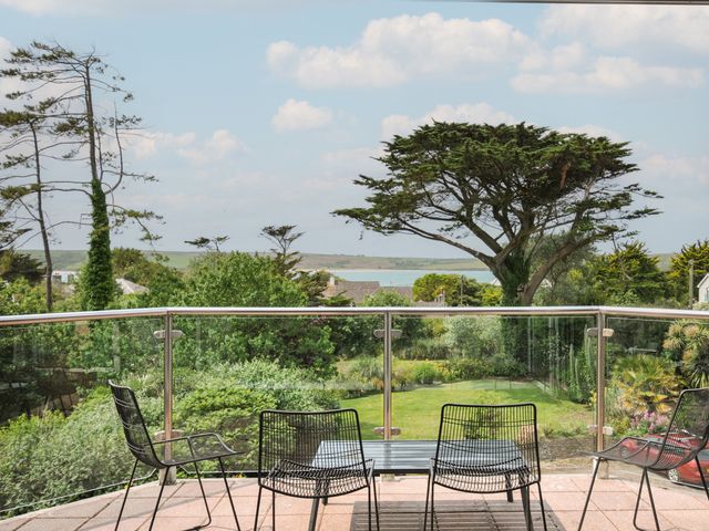 An outdoor balcony with chairs and a table overlooking a garden at Bodare 8 in Daymer Bay