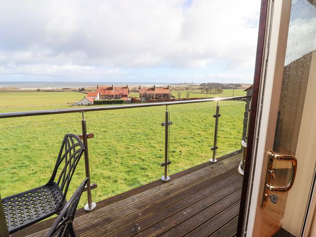 A balcony with black chairs overlooking green fields and houses near the coast at Waters Edge in Embleton