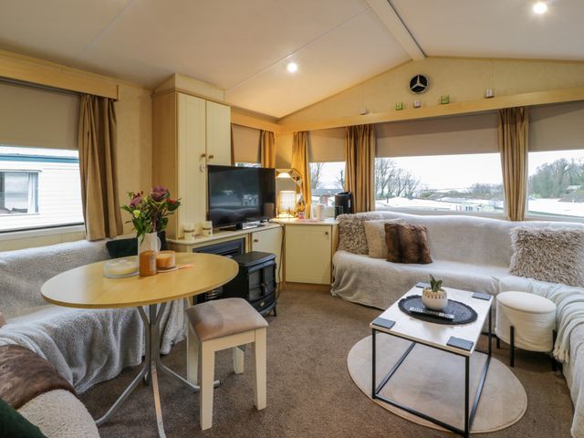 A living room with a corner sofa a round dining table a small fireplace and a television at Seaviews in Cairnryan near Stranraer