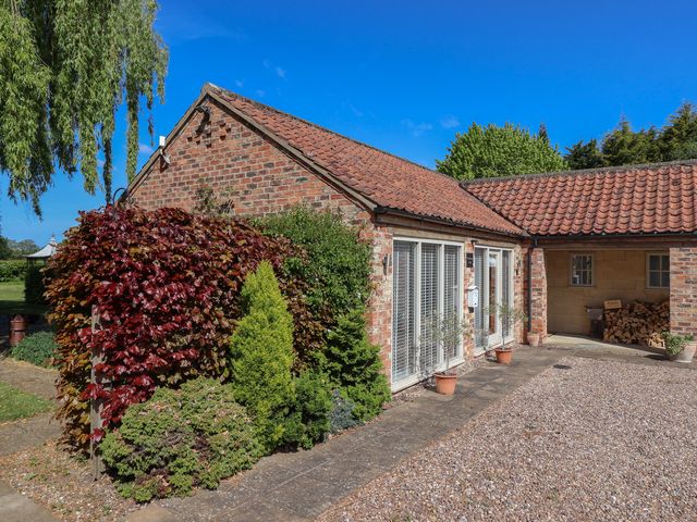 A brick house with a tiled roof surrounded by bushes and potted plants near a gravel driveway at Providence Court Near Easingwold