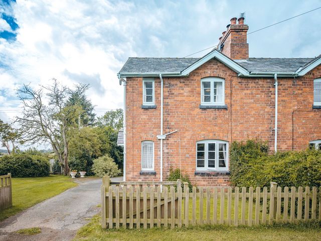 A brick house with white framed windows and a wooden fence in front at Shepherd's Cottage in Eudon Burnell near Bridgnorth