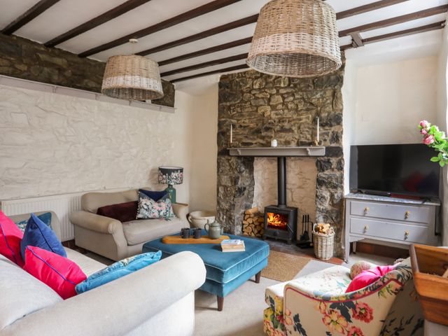 A living room with a stone fireplace a wood stove sofas with colorful cushions an ottoman and a TV on a cabinet at Riverwash Cottage in Dwygyfylchi