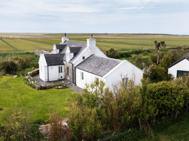 A white house with multiple chimneys surrounded by green fields and bushes at Taigh Phinc Balemore near Lochmaddy North Uist