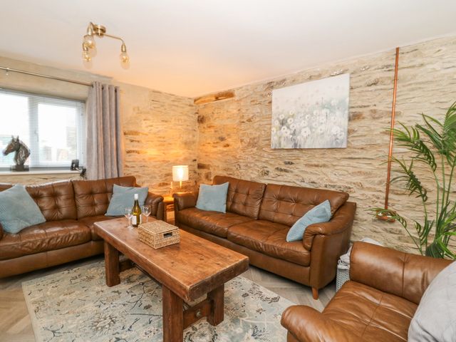 A living room with brown leather sofas a wooden table and stone walls at La Bastille in Maenclochog