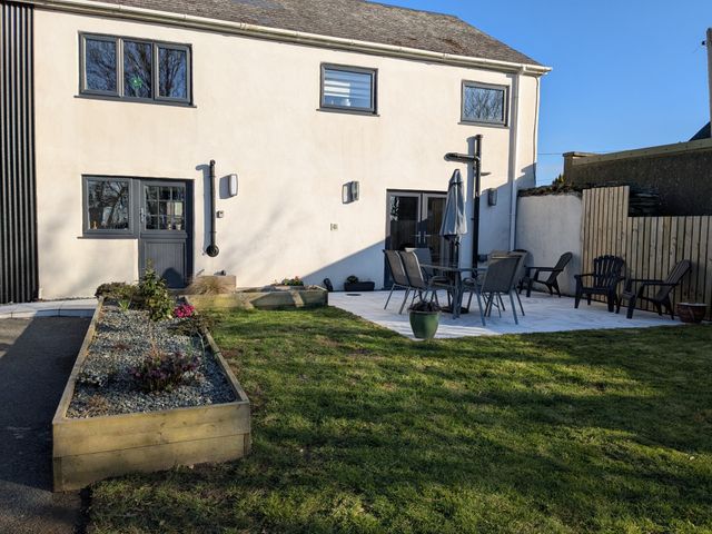 A garden with grass and a raised flower bed beside a white building with outdoor furniture and a patio at La Bastille in Maenclochog