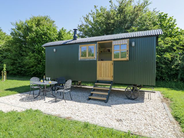 A green shepherd hut on gravel with a small black metal table and three chairs outside at Spindle South Leigh near Witney