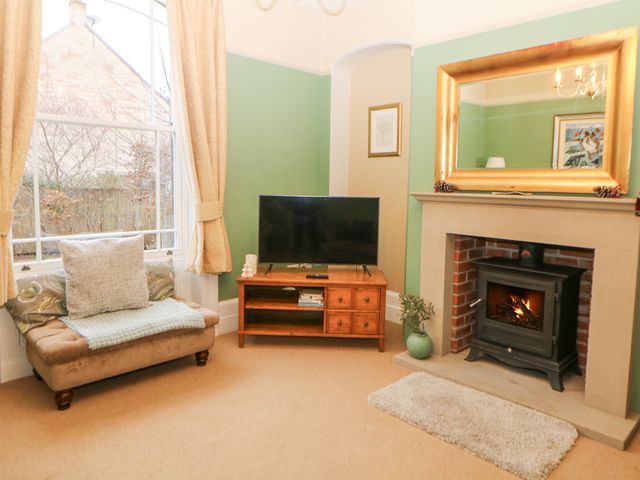 A living room with a fireplace a television on a wooden stand and a cushioned bench by a window at Deeley House in Darley Dale