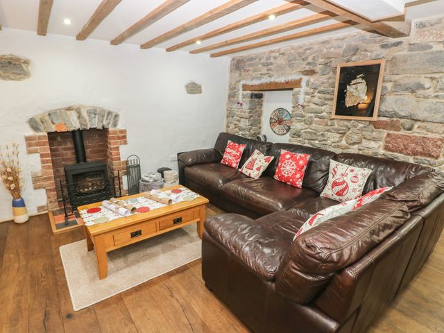 A living room with a brown leather corner sofa and a wooden coffee table in front of a fireplace set in a white and stone wall at Blacksmiths Cottage in Pembroke
