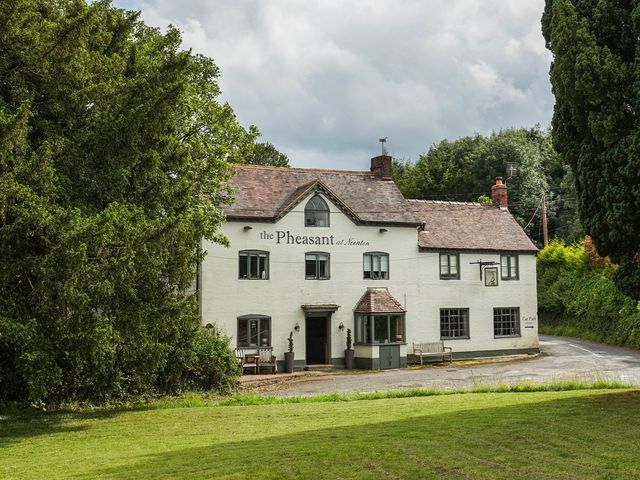 A white building with windows and a sign reading the Pheasant at Neenton surrounded by trees and grass
