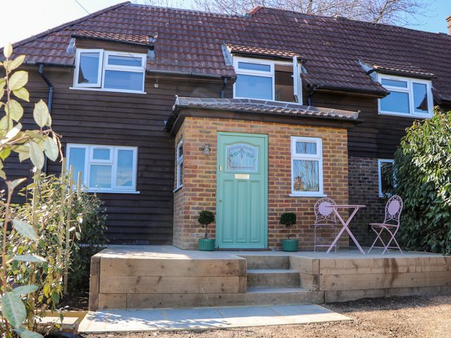 Front of a house with a green door small round table and two chairs on a wooden deck at Hyrst Rise in Forest Row