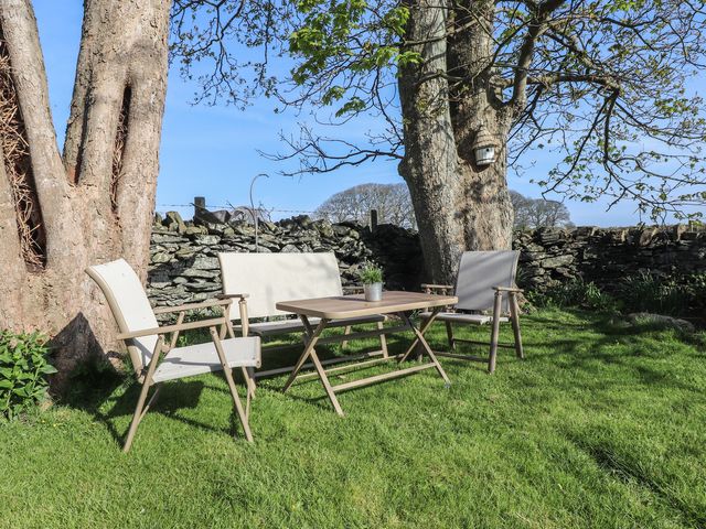 An outdoor seating area with a table three chairs and large trees in a garden at 5 Stad Clynnog Dwyran near Niwbwrch newborough