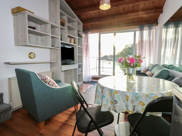 A living room with armchairs a round table with flowers and a wall unit with a television at Seafarer's Haven in Porthmadog