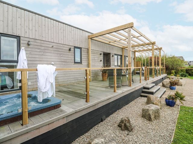A wooden deck with glass railing and a blue hot tub beside a wooden house at Petroc in Portreath