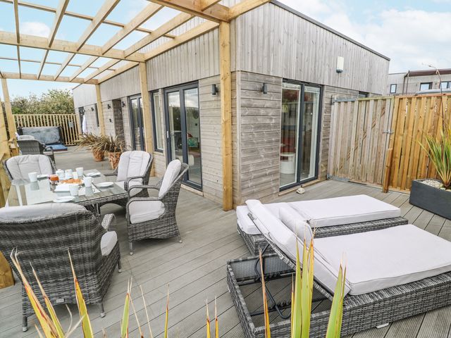 An outdoor patio with wicker chairs and loungers on a wooden deck at Petroc in Portreath