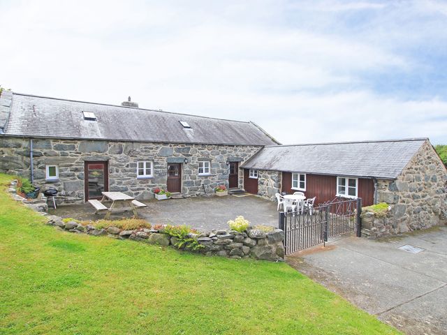 A stone cottage with a slate roof and patio furniture in a gated yard at Y Stabl The Old Stable in Llanbedr