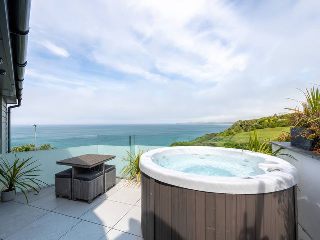 An outdoor space with a hot tub and table overlooking the ocean at 7 Atlantic Watch in Carbis Bay