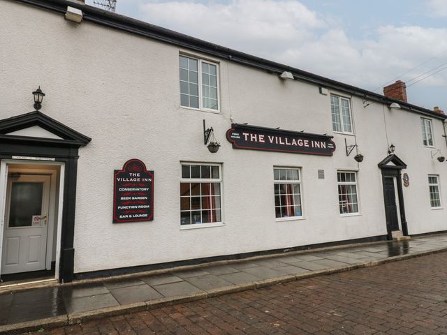 The exterior of The Village Inn with several windows doors and signs on a paved street at Sycamore Room in Murton