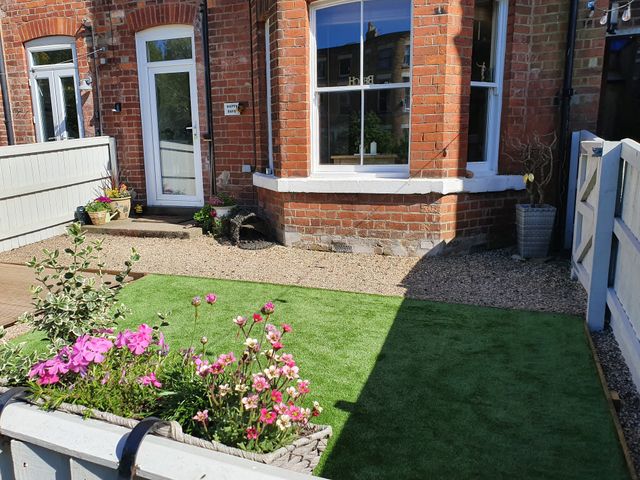 A small garden with flowers and artificial grass in front of a brick house with white doors and windows at Happy Days in Scarborough