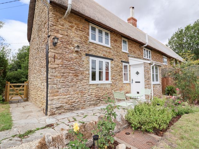 A house with a thatched roof and garden furniture at Thatchers End in Sherborne