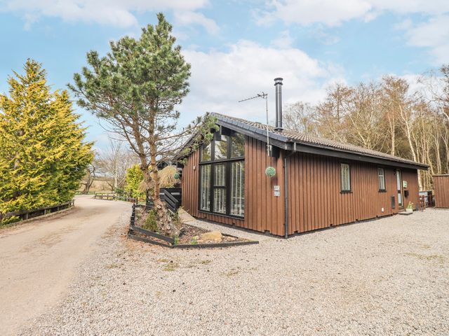 A brown building with windows and trees at Fig Tree Lodge, Hutton Roof near Penrith