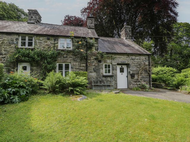 A cottage with a door and windows surrounded by grass and plants at Glandwr Cottage Llanbedr
