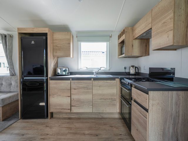 A kitchen with wooden cabinets a black refrigerator a toaster a kettle a stove and a window at The Splash Pad - Billing Aquadrome in Billing Aquadrome Holiday Park